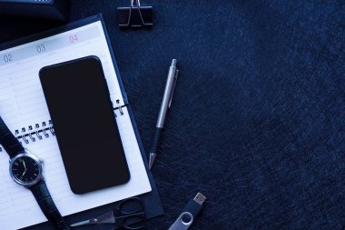 Siyah ofis malzemeleri: kaplıcada haftalık açık saat, kalem, klips, makas, flaş bellek ve siyah arka planda akıllı telefon. Düz plan. Yukarıdan bak. Metin için boşluk