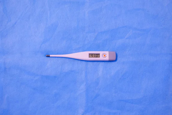 electronic thermometer lies on a blue background. thermometer displays high temperature