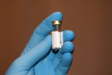 Tıbbi eldivenin içinde aşıyla dolu bir şişe var. Kahverengi arkaplandaki fotoğraf