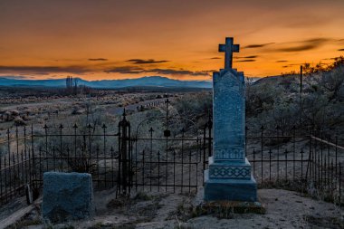 Gökyüzü sıcacık renklerle dolu bir mezarlık haçı ötesinde