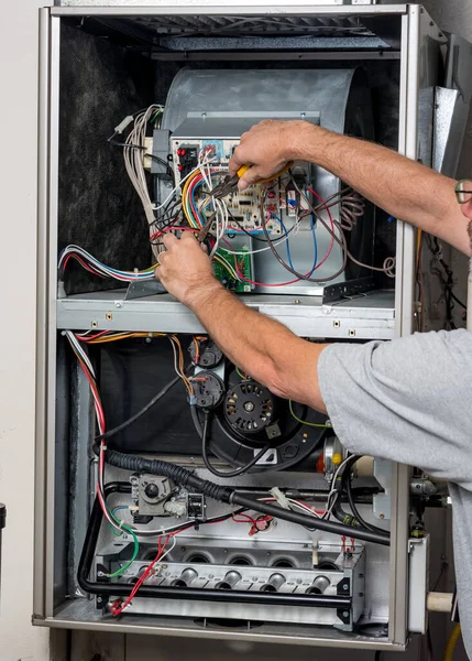 Man works with the wires on circuit boards of a home furnace