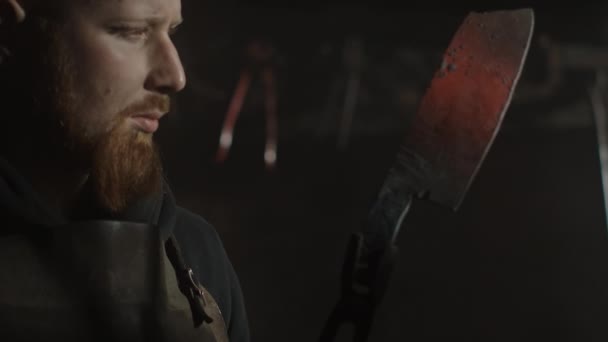 Retrato de um ferreiro aperfeiçoando sua lâmina em um interior escuro de sua oficina de metal . — Vídeo de Stock