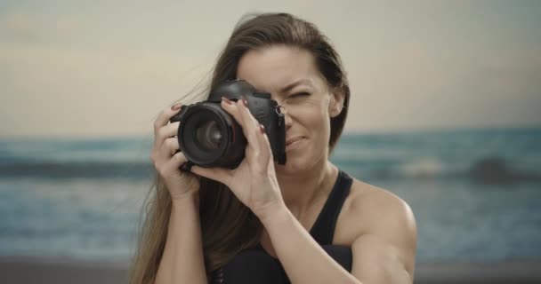 Vrouwenfotografe die haar Dslr-camera op het strand gebruikt. Zee op de achtergrond. Langzame beweging 4k — Stockvideo