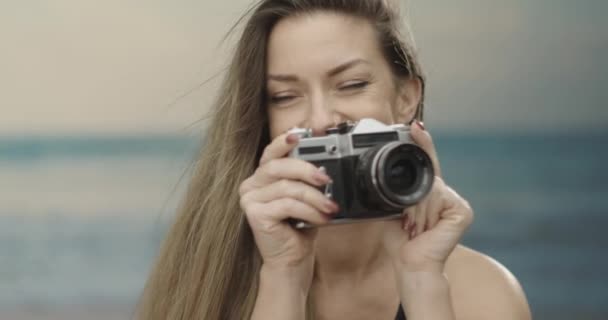 Linda fotógrafa femenina usando su cámara analógica en la playa. Mar en el fondo. cámara lenta 4K — Vídeos de Stock