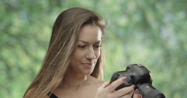 Fotógrafa femenina linda utilizando su cámara réflex digital en nature.trees en el fondo. cámara lenta 4K — Vídeos de Stock