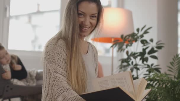 Schöne junge Frau liest ein Buch in einem gemütlichen Wohnzimmer. — Stockvideo
