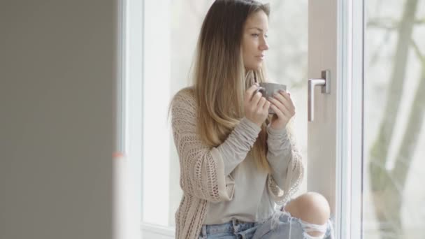 Vacker brunett dricka kaffe och titta genom ett fönster i hennes nya hem. — Stockvideo