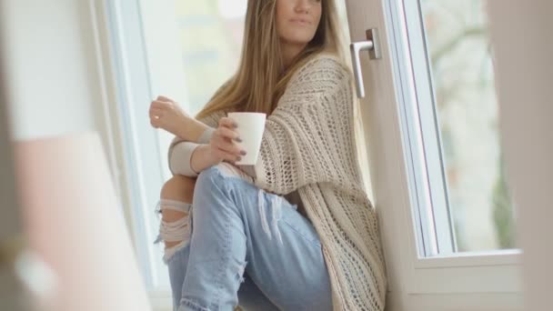 Όμορφη νεαρή γυναίκα πίνοντας τσάι και κοιτάζοντας μέσα από ένα παράθυρο του νέου της σπιτιού. — Αρχείο Βίντεο
