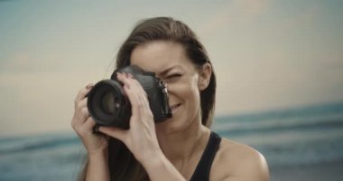 Kumsalda fotoğraf makinesi kullanan hoş bir kadın fotoğrafçı. Arka planda deniz. Yavaş çekim 4k