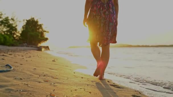 Mezítlábas nő egy nyári ruha sétál a strandon, a tenger a naplementében. — Stock videók