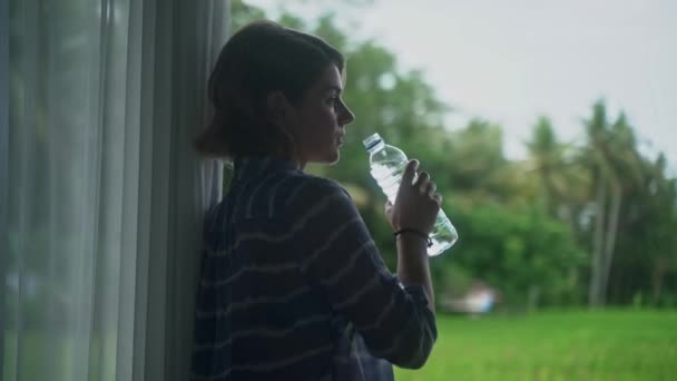 Bela mulher caucasiana beber água engarrafada em seu alpendre com uma bela vista vívida da natureza . — Vídeo de Stock