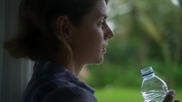 Doe dicht. mooie Kaukasische vrouw drinken gebotteld water op haar veranda met een prachtig levendig uitzicht op de natuur. — Stockvideo