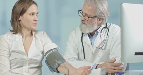 Médico en su consultorio midiendo la presión arterial de su paciente femenino — Vídeos de Stock