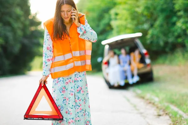 Woman in orange reflective vest installing red warning triangle — 图库照片