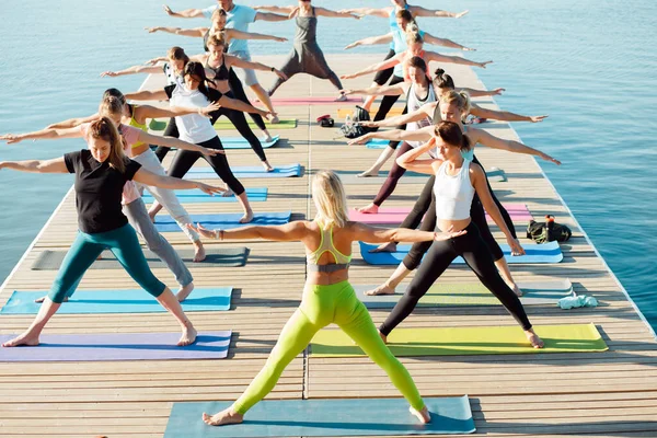 Gölün yakınındaki bir pontonda yoga derslerine katılan büyük bir grup insan..