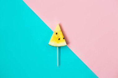 Pembe-mavi arka planda üç köşeli olgun sarı karpuz dilimini kes.