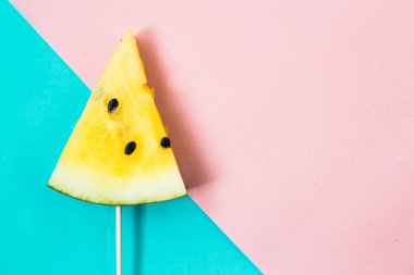 Pembe-mavi arka planda üç köşeli olgun sarı karpuz dilimini kes.