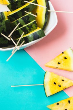 Pembe-mavi arka planda olgun sarı karpuz dilimlerini kes.