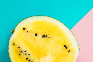 Pembe-mavi arka planda olgun sarı yarım karpuz kesilmiş.