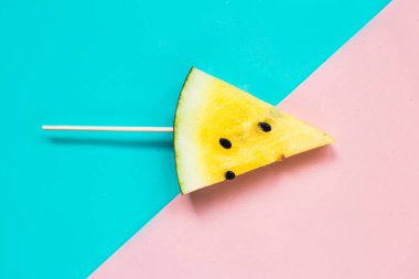 Pembe-mavi arka planda üç köşeli olgun sarı karpuz dilimini kes.