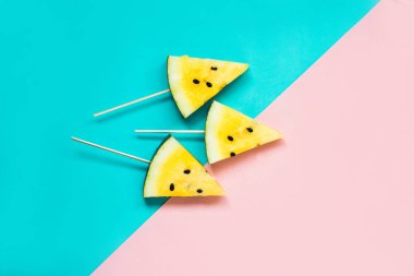 Pembe-mavi arka planda olgun sarı karpuz dilimlerini kes.