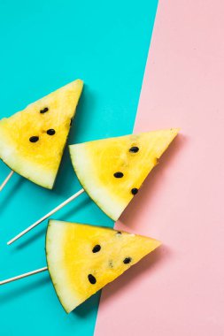 Pembe-mavi arka planda olgun sarı karpuz dilimlerini kes.