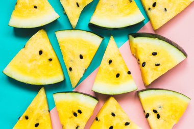 Pembe-mavi arka planda olgun sarı karpuz dilimlerini kes.