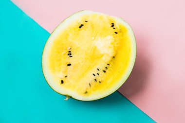 Pembe-mavi arka planda olgun sarı yarım karpuz kesilmiş.