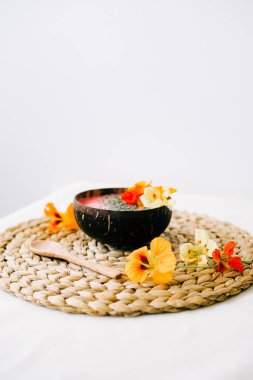 Hindistancevizi tabağında sağlıklı bir kahvaltı ve doğal hasır peçetede nasturtiyum çiçekli bambu kaşığı.