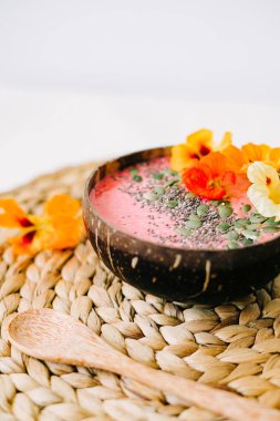 Hindistancevizi tabağında sağlıklı bir kahvaltı ve doğal hasır peçetede nasturtiyum çiçekli bambu kaşığı.