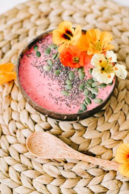 Hindistancevizi tabağında sağlıklı bir kahvaltı ve doğal hasır peçetede nasturtiyum çiçekli bambu kaşığı.