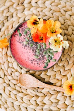 Hindistancevizi tabağında sağlıklı bir kahvaltı ve doğal hasır peçetede nasturtiyum çiçekli bambu kaşığı.