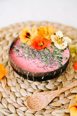 Hindistancevizi tabağında sağlıklı bir kahvaltı ve doğal hasır peçetede nasturtiyum çiçekli bambu kaşığı.