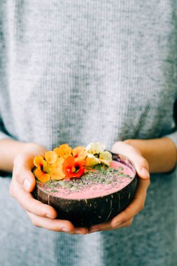 Hindistan cevizi kasesinde sağlıklı bir kahvaltı. Beyaz arka planda, elinde nasturtium çiçekleri var.