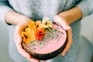 Hindistan cevizi kasesinde sağlıklı bir kahvaltı. Beyaz arka planda, elinde nasturtium çiçekleri var.