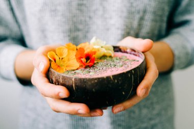 Hindistan cevizi kasesinde sağlıklı bir kahvaltı. Beyaz arka planda, elinde nasturtium çiçekleri var.