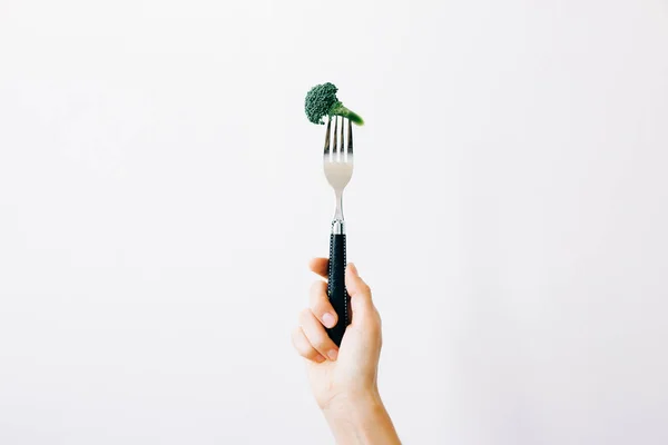 Mano che tiene una forchetta con un'infiorescenza verde di broccoli freschi su fondo bianco. cibo vegano — Foto Stock
