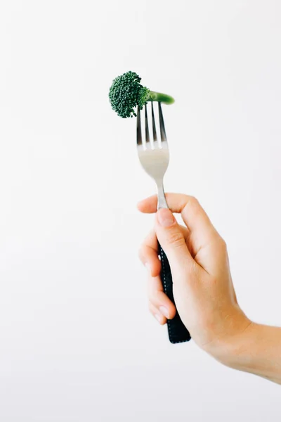 Mano che tiene una forchetta con un'infiorescenza verde di broccoli freschi su fondo bianco. cibo vegano — Foto Stock