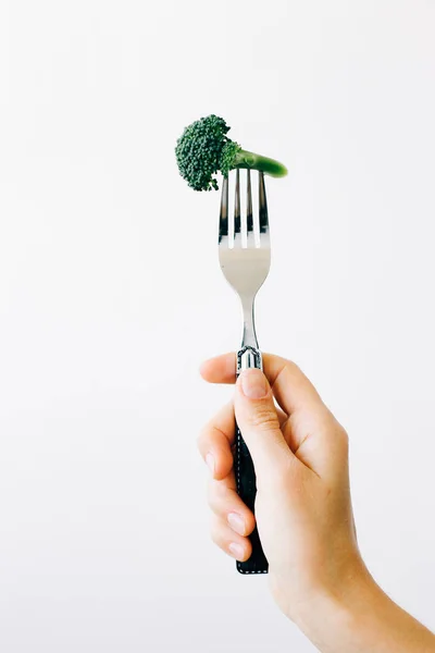 Mano che tiene una forchetta con un'infiorescenza verde di broccoli freschi su fondo bianco. cibo vegano — Foto Stock