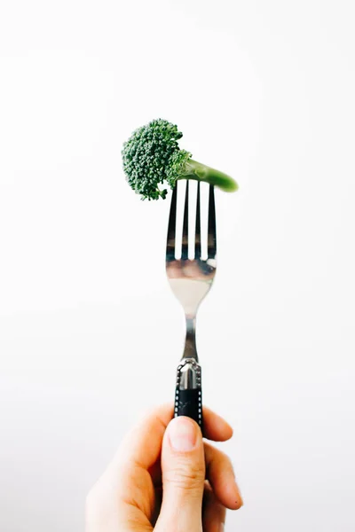 Mano che tiene una forchetta con un'infiorescenza verde di broccoli freschi su fondo bianco. cibo vegano — Foto Stock