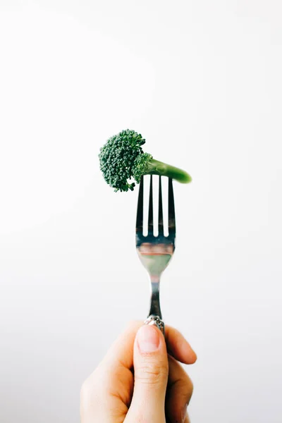 Mano che tiene una forchetta con un'infiorescenza verde di broccoli freschi su fondo bianco. cibo vegano — Foto Stock