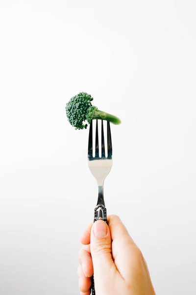 Mano che tiene una forchetta con un'infiorescenza verde di broccoli freschi su fondo bianco. cibo vegano — Foto Stock