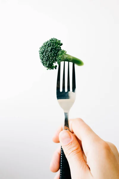 Mano che tiene una forchetta con un'infiorescenza verde di broccoli freschi su fondo bianco. cibo vegano — Foto Stock