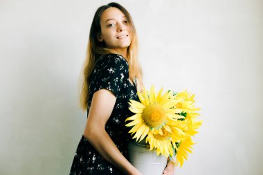 Beyaz arka planda ayçiçeği çiçekli sarı bir vazo tutan genç tatlı bir kız.