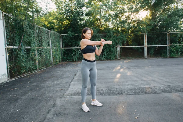 Una chica guapa joven en el patio de recreo en ropa deportiva hace ejercicios físicos. en el verano al atardecer —  Fotos de Stock