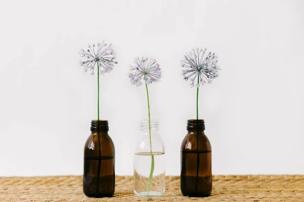 three purple round flowers in glass jars a wicker table