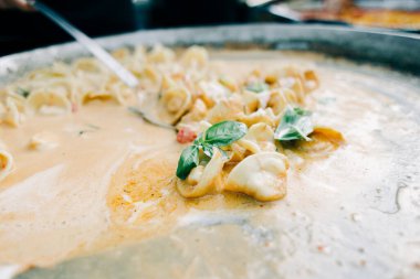 Lezzetli ravioli, domatesli ve kremalı soslu fesleğen, büyük bir tavada, sokak yemeği.