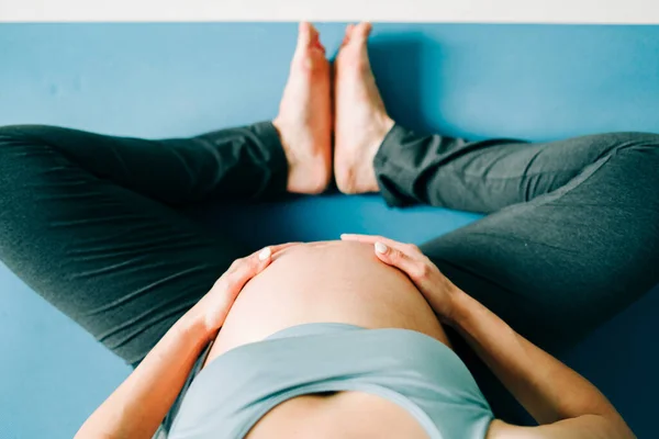 a young pretty pregnant girl in sports clothes is doing yoga, doing asana Baddha Konasana on the Mat, top view