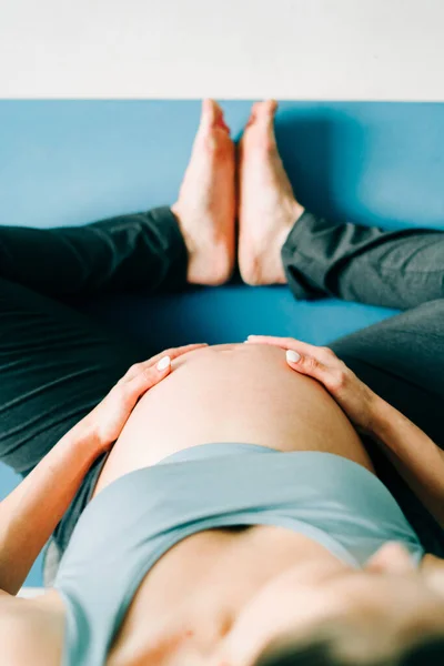 a young pretty pregnant girl in sports clothes is doing yoga, doing asana Baddha Konasana on the Mat, top view