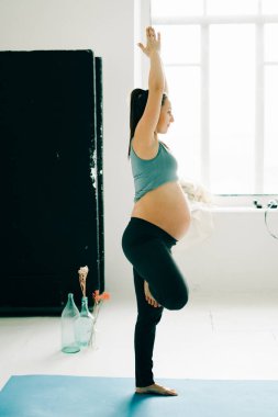 a young pretty pregnant girl in sports clothes is doing yoga, doing asana on the Mat in the Studio